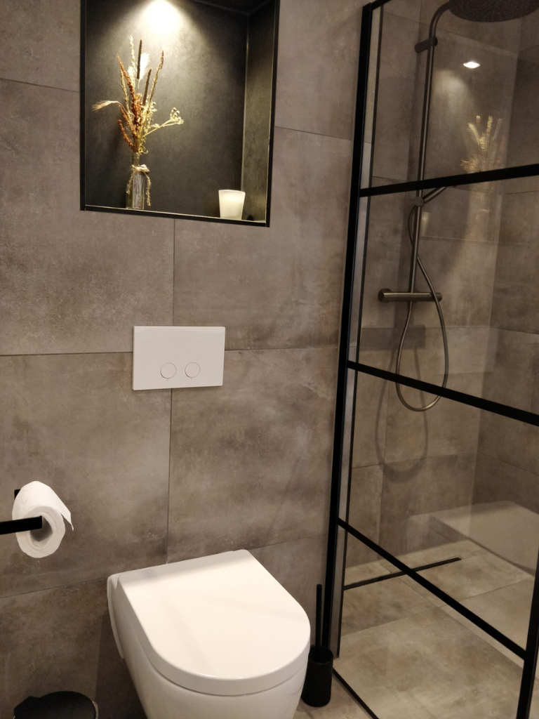 Toilet en douche met betonlook tegels en zwart stalen profiel